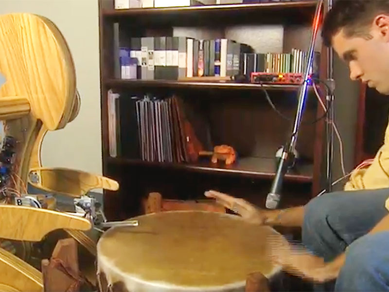 Drumming robot plays a bongo with a human student.